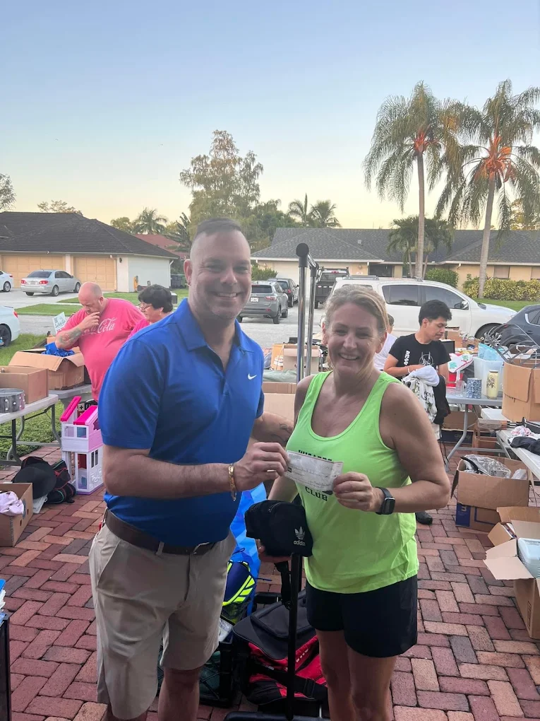 Man in blue polo and woman in green tank top smiling at outdoor garage sale event
